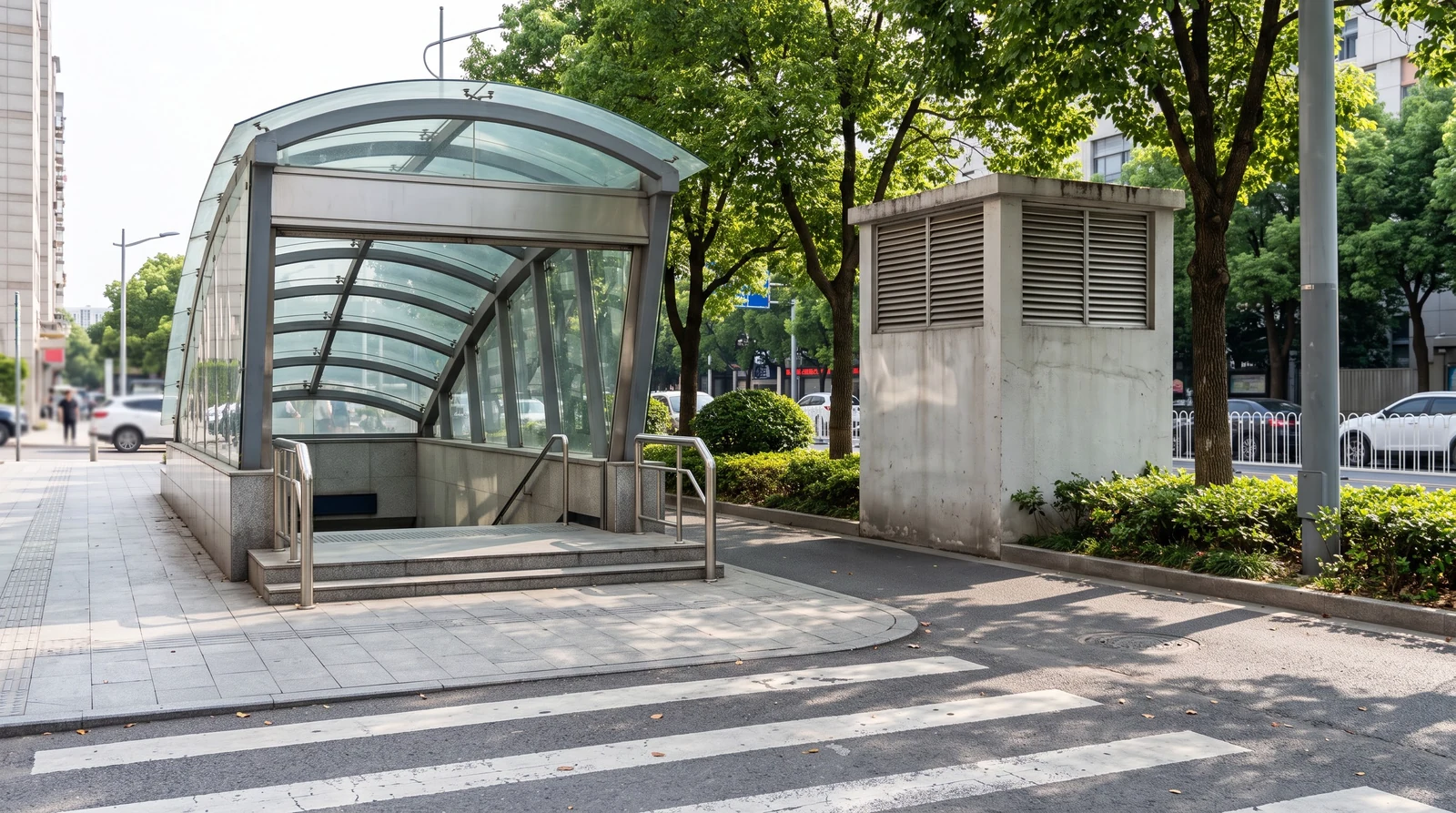 城市街道边的地铁出入口,带玻璃顶棚的台阶通入地下,旁边有一座方形风亭
